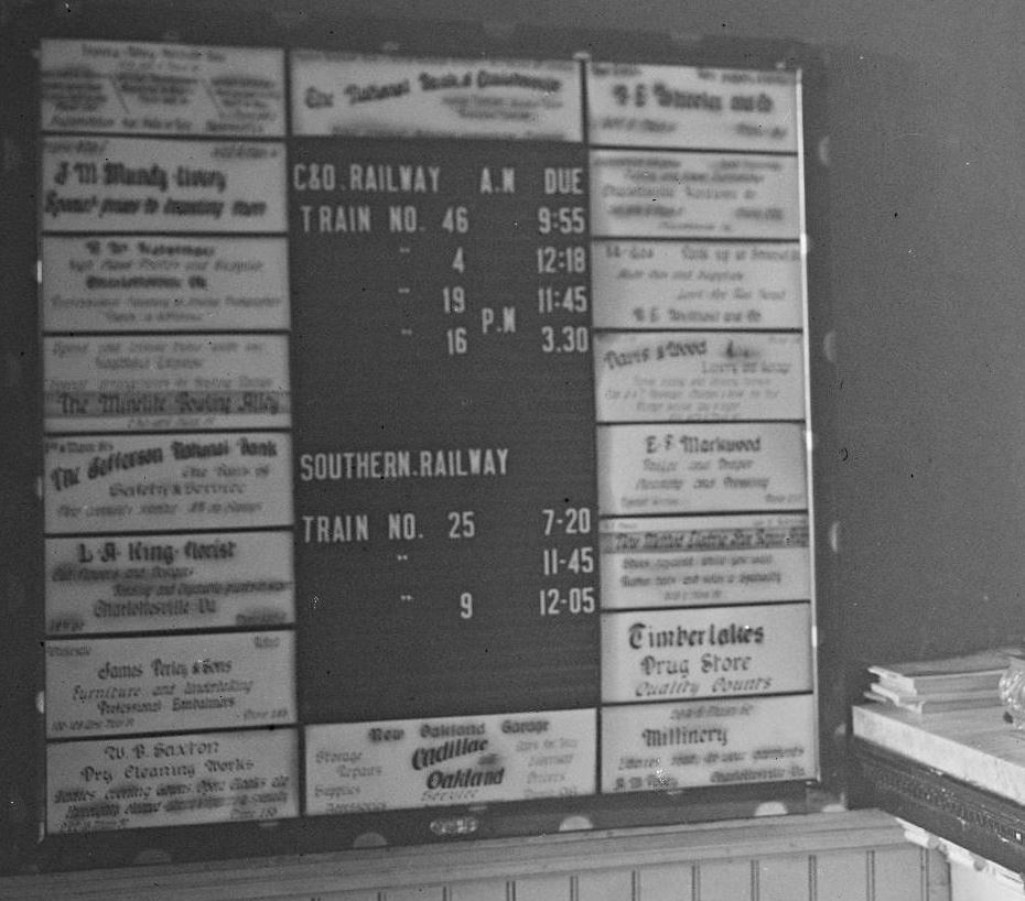 Hand-lettered advertisements for local businesses surround the Charlottesville train timetable in the Gleason Hotel in 1915, detail from a larger photograph. photograph from 
