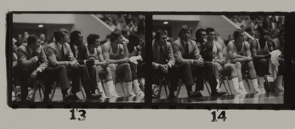 Black and white photograph of Coach Terry Holland and other coaches and players sitting on bench. 