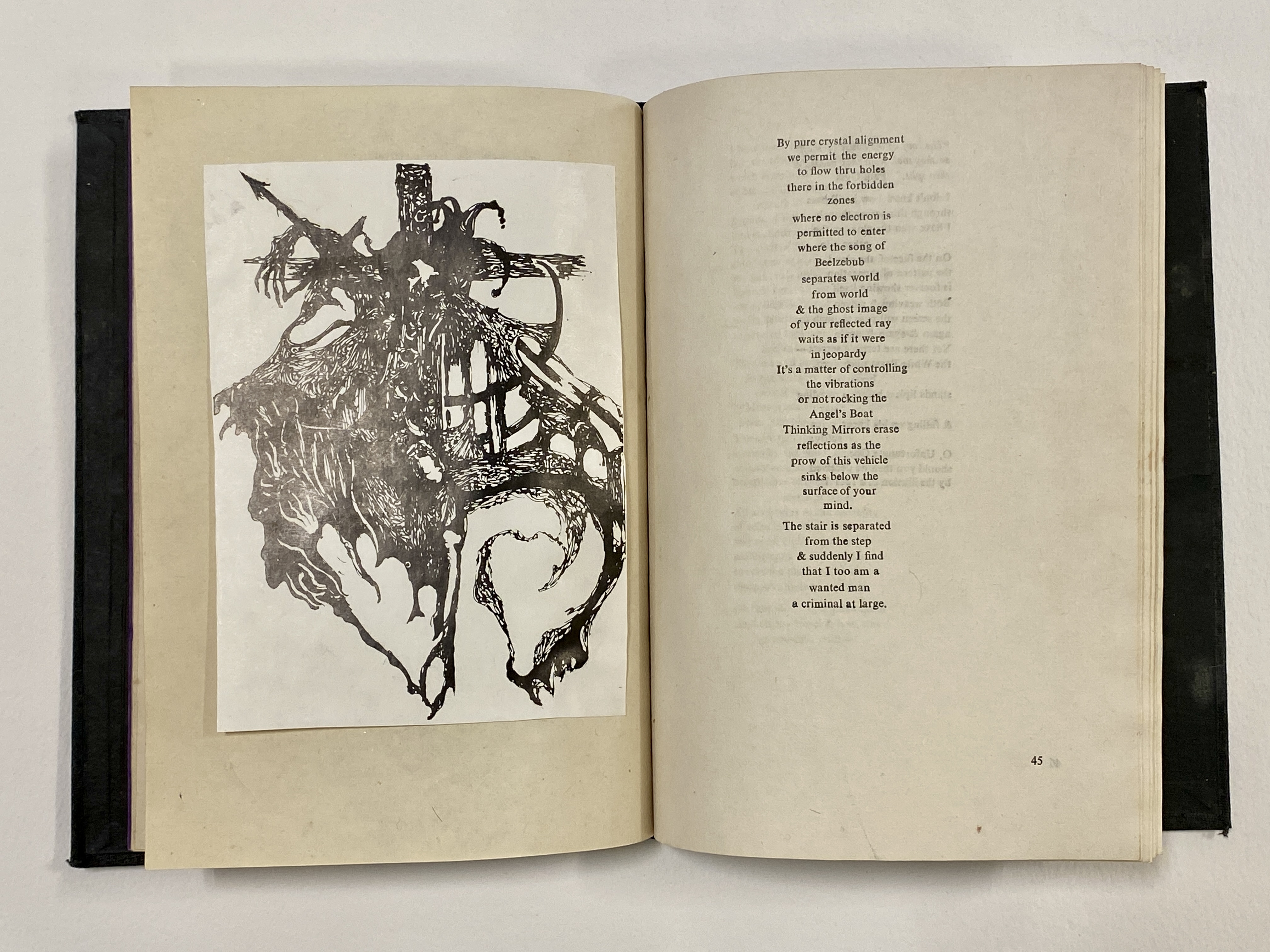 A hardcover book with black endpapers is open on a table. It is open to a page spread with a mounted print of a drawing on the verso, and a narrow column of verse on the recto.